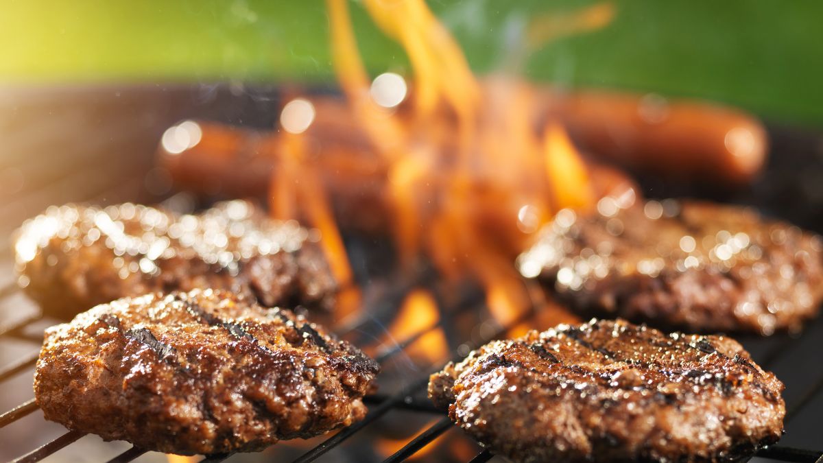 Grillezett hamburgerek és virslik sülnek a parázson, ínycsiklandó látvány.