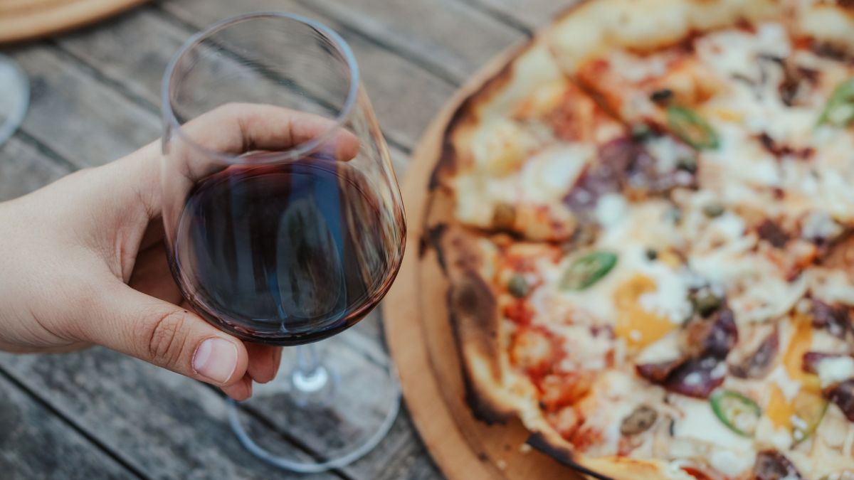 Egy pohár vörösbor és egy ízletes pizza egy fából készült asztalon.