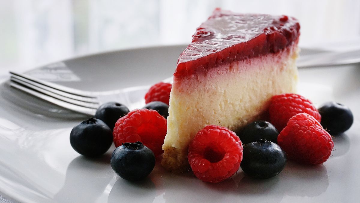 Egy szelet gyümölcsös sajttorta, friss málnával és áfonyával díszítve.