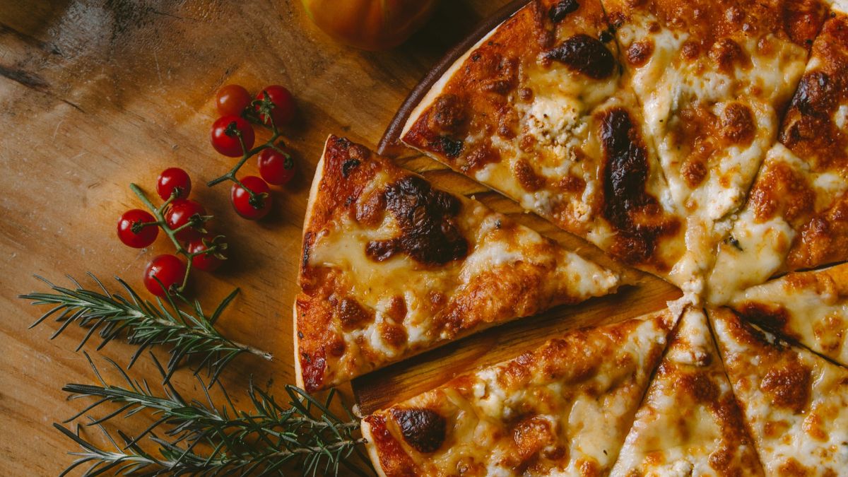 Frissen sült házi pizza, ropogós peremmel és olvadt sajttal, körülötte paradicsom és rozmaring.